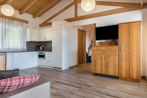 A modern kitchen with white cabinets, a wooden dining table, and a TV mounted on the wall.