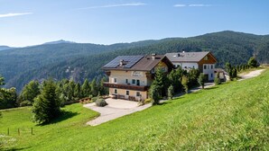 Ein zweistöckiges Berggrundstück mit Solaranlage, Terrasse und Blick auf bewaldete Berge.