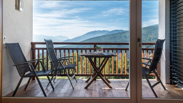 Ein Balkon mit Tisch und Stühlen, Holzgeländern und Blick auf Berge.