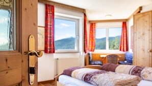A wooden-framed room with a bed, a window with curtains, and a view of mountains. - Apartment 'Apt Gaisler' with Mountain View, Private Terrace and Wi-Fi (Maranza)