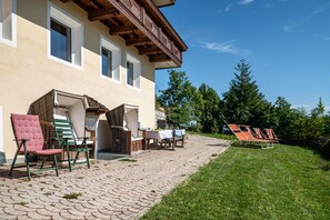 Un bâtiment doté d’un patio dallé, d’un espace extérieur aménagé avec des sièges et d’une pelouse avec des chaises longues.