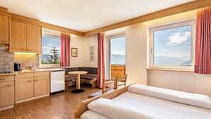 A compact hotel room with a kitchenette, a bed, a small dining table, and a window with a mountain view.