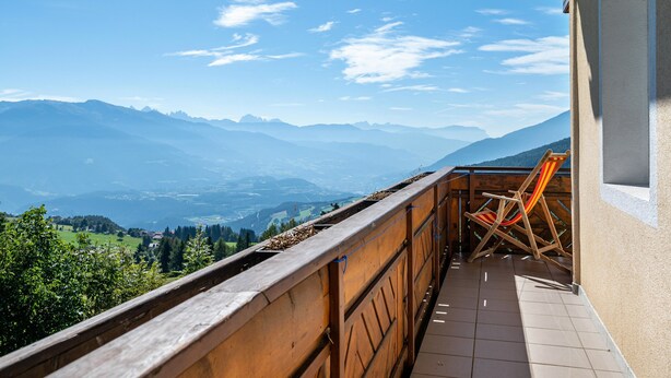 A balcony with a wooden railing, a chair, and a view of mountains and valleys.