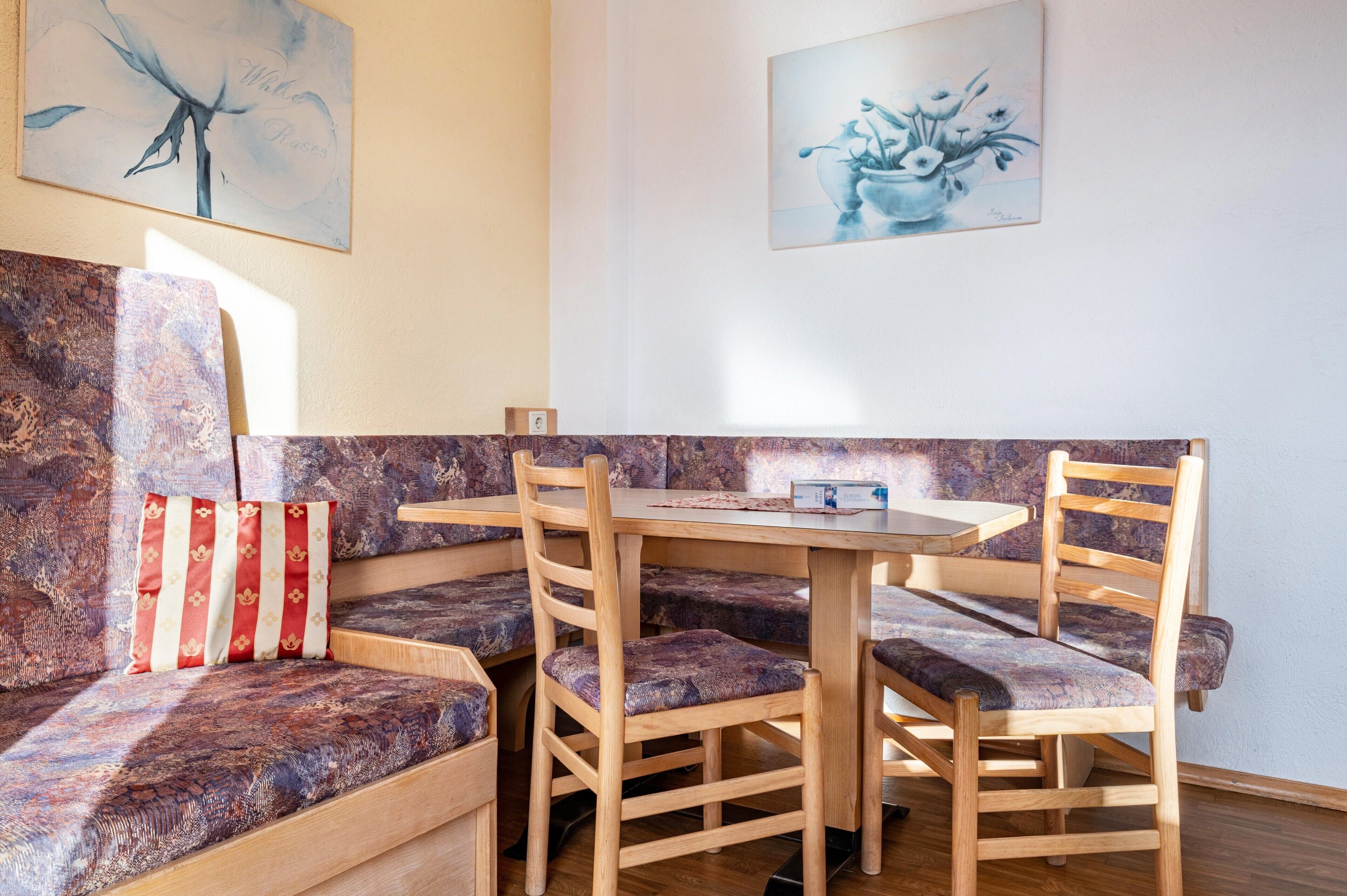 A dining area with a wooden table and chairs, a cushioned bench, and two wall-mounted artworks.