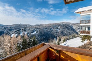 En träveranda med utsikt över ett snöklätt berglandskap, och en modern byggnad i förgrunden med stora fönster och en balkong.