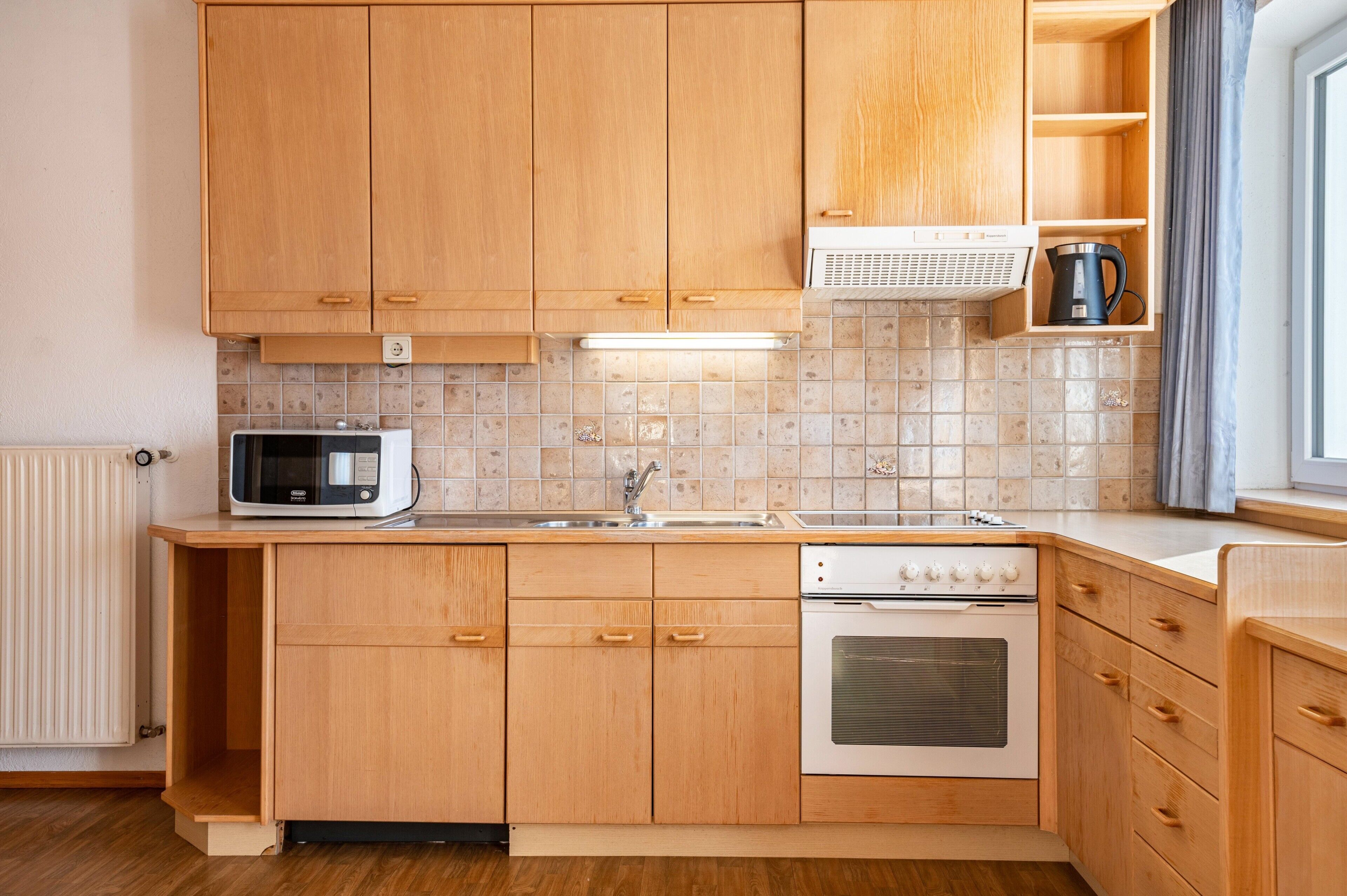Una cucina con mobili in legno, un forno a microonde, un lavello, un fornello e un bollitore.