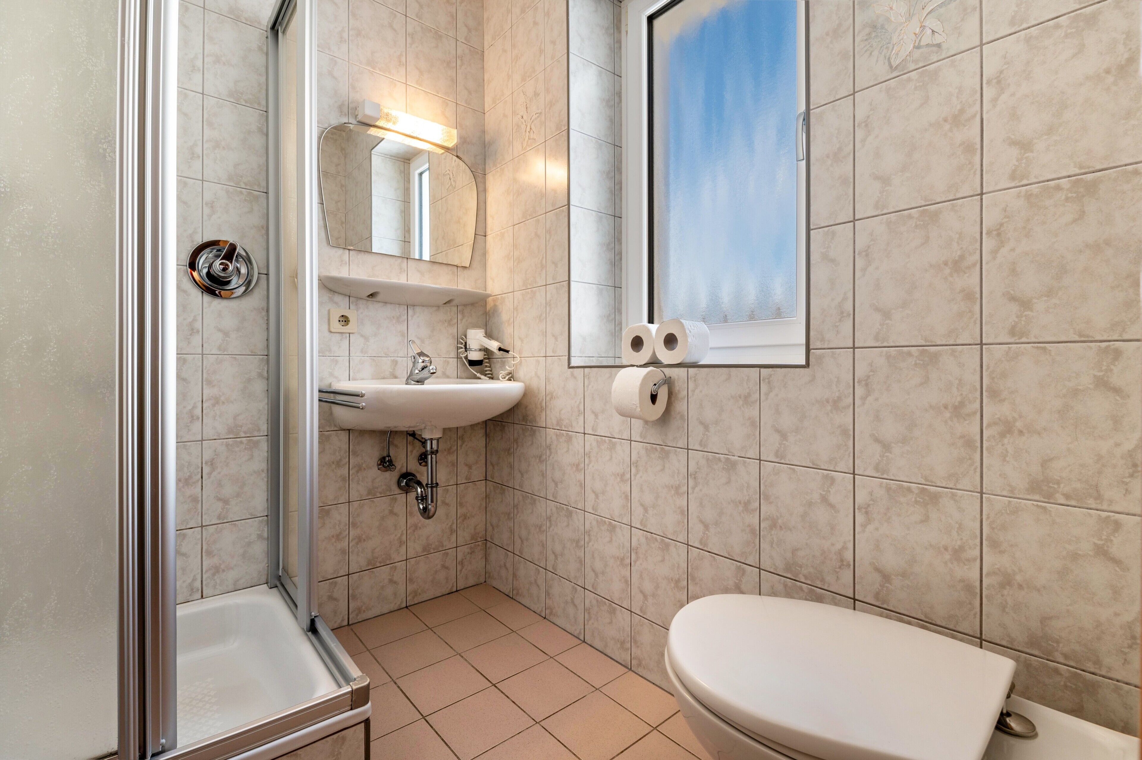 Une salle de bain avec douche, lavabo, toilettes et une fenêtre donnant sur un beau paysage.