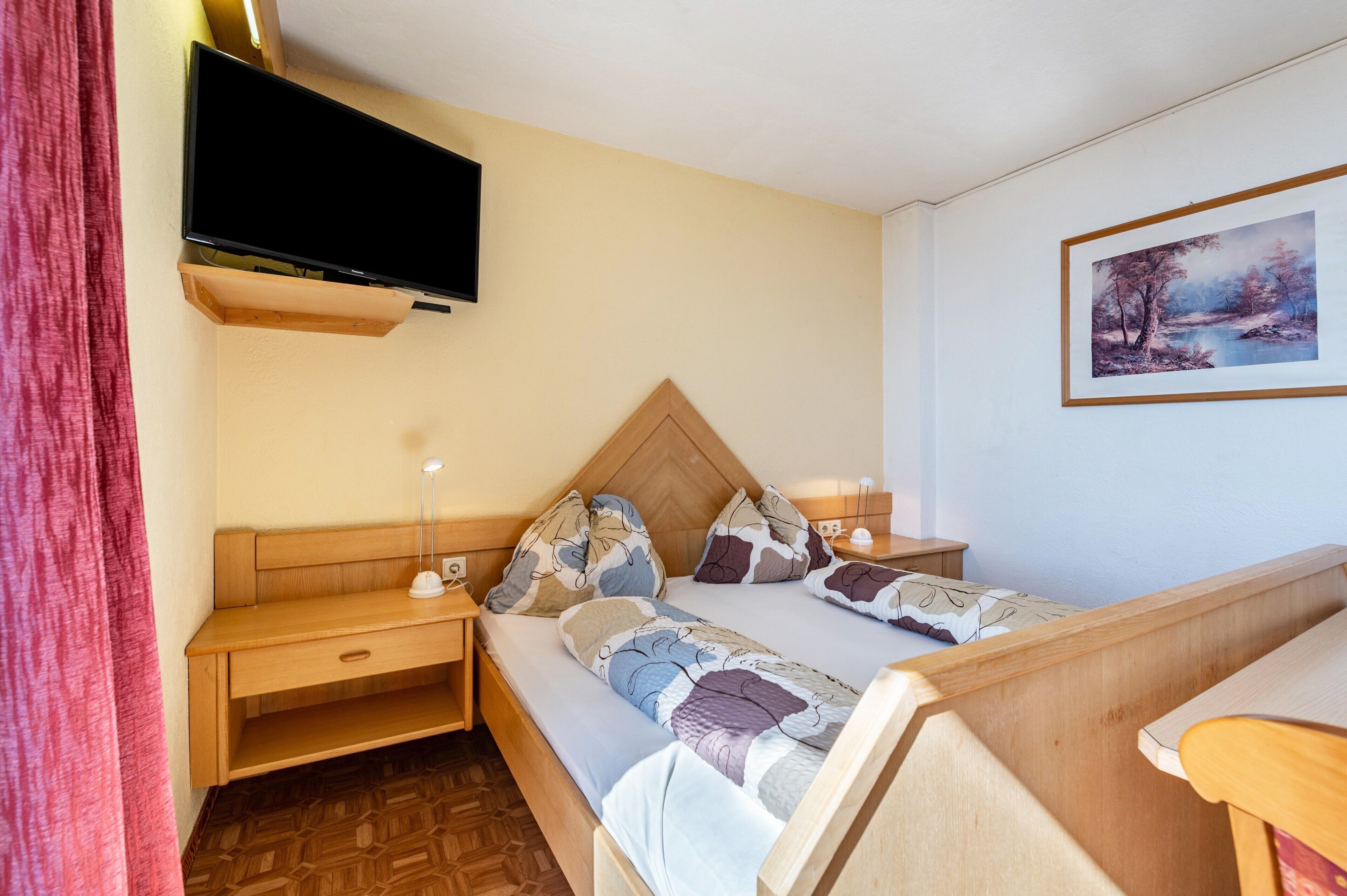 Une chambre à coucher avec un lit, un bureau, une télévision et un tableau accroché au mur.