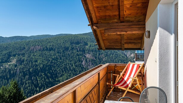 A balcony with a wooden railing, a table, and a red and white striped beach chair. - Cozy Waldblick Apartment with Mountain Views & Terrace in Meransen (Maranza)