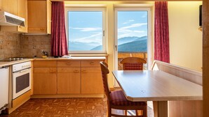 A kitchen with wooden cabinets, a stove, and a window with a view of mountains. - Cozy Waldblick Apartment with Mountain Views & Terrace in Meransen (Maranza)