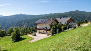 A two-story mountain house with solar panels, a patio, and a view of the forested mountains. - Cozy Waldblick Apartment with Mountain Views & Terrace in Meransen (Maranza)