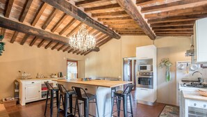 A kitchen with a central island, bar stools, a chandelier, and modern appliances. - Holiday Apartment 'Glicine' with Mountain View, Shared Pool & Wi-Fi (Montieri)