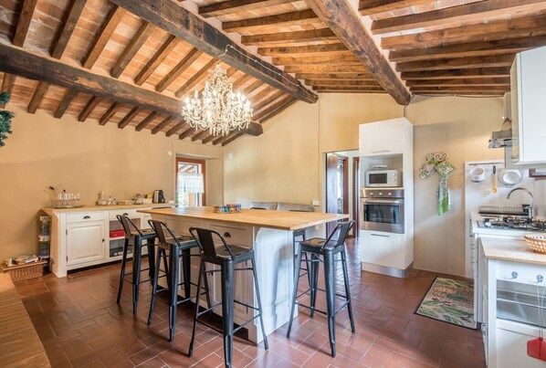 A kitchen with a central island, bar stools, a chandelier, and modern appliances.