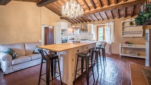 A spacious kitchen with a wooden island, bar stools, a chandelier, and a white sofa. - Holiday Apartment 'Glicine' with Mountain View, Shared Pool & Wi-Fi (Montieri)