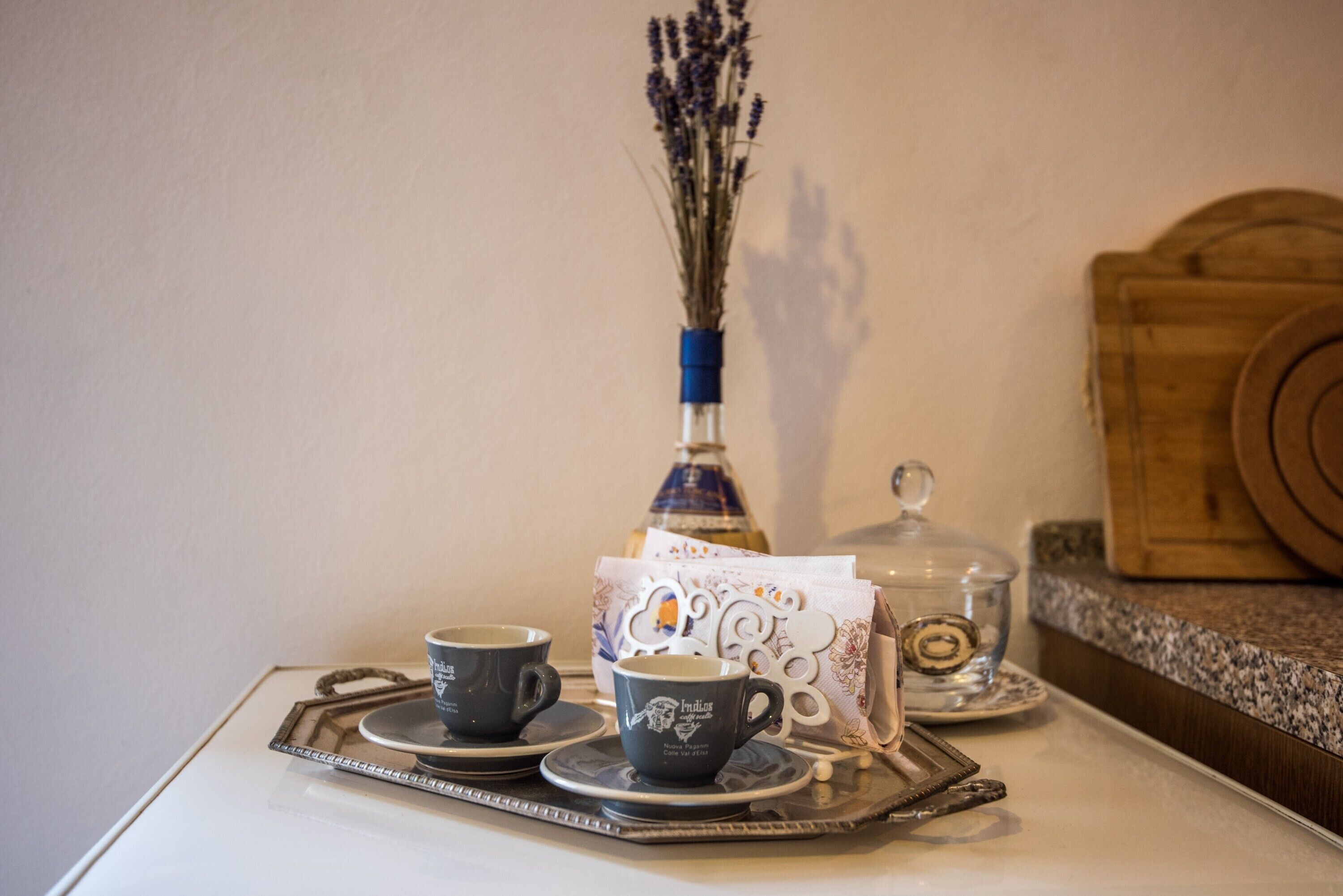 A tray with two cups, a vase with dried flowers, and a glass container on a table.
