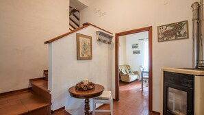 Una escalera con barandilla de madera, una pequeña mesa redonda con una vela, una silla blanca, una chimenea y un comedor con una silla y una mesa al fondo.