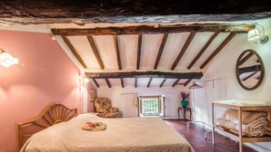 Un dormitorio con techo de madera, una cama con almohada estampada, una silla, una mesita y un estante con mantas dobladas.
