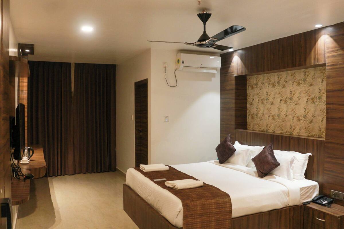 A hotel room with a bed, a ceiling fan, an air conditioning unit, a bedside table, and a telephone.
