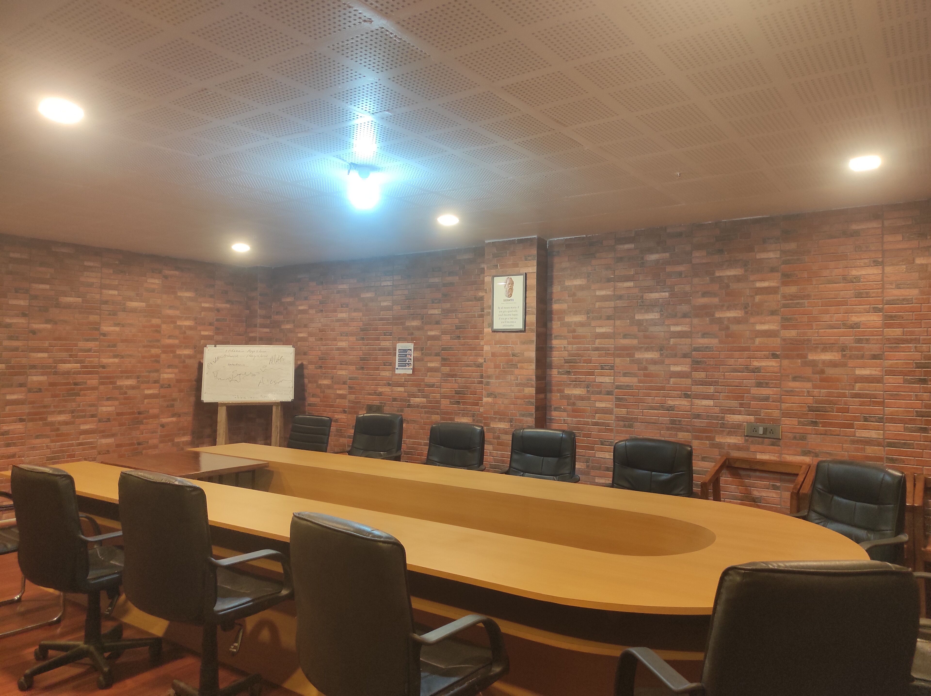 A conference room with a long table, black chairs, a whiteboard, and a brick wall.