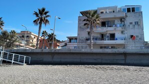 Un edificio de varios pisos con balcones, una playa al frente y palmeras.
