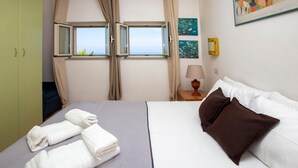 Habitación de hotel con cama, dos toallas enrolladas, mesita de noche con lámpara, ventana con cortinas y decoración en la pared.
