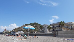 Una playa con sombrillas, un faro y edificios al fondo.