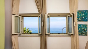 Una habitación con vista al mar a través de una ventana con cortinas.