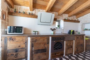 A kitchen with wooden cabinetry, a built-in oven, a microwave, and a stone wall.