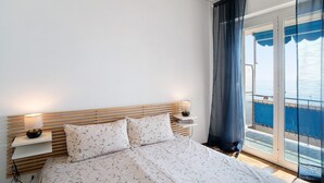 A bedroom with a bed, bedside lamps, a nightstand, and a view through a glass door. - Holiday Apartment 'Margherita' with Sea View, Balcony & Wi-Fi (Ospedaletti)