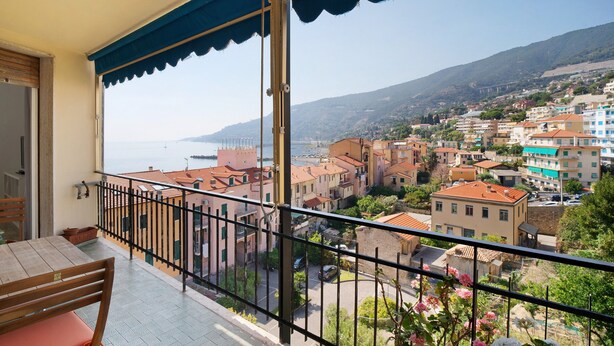 A balcony with a view of a coastal town, a table with chairs, and a railing. - Holiday Apartment 'Margherita' with Sea View, Balcony & Wi-Fi (Ospedaletti)