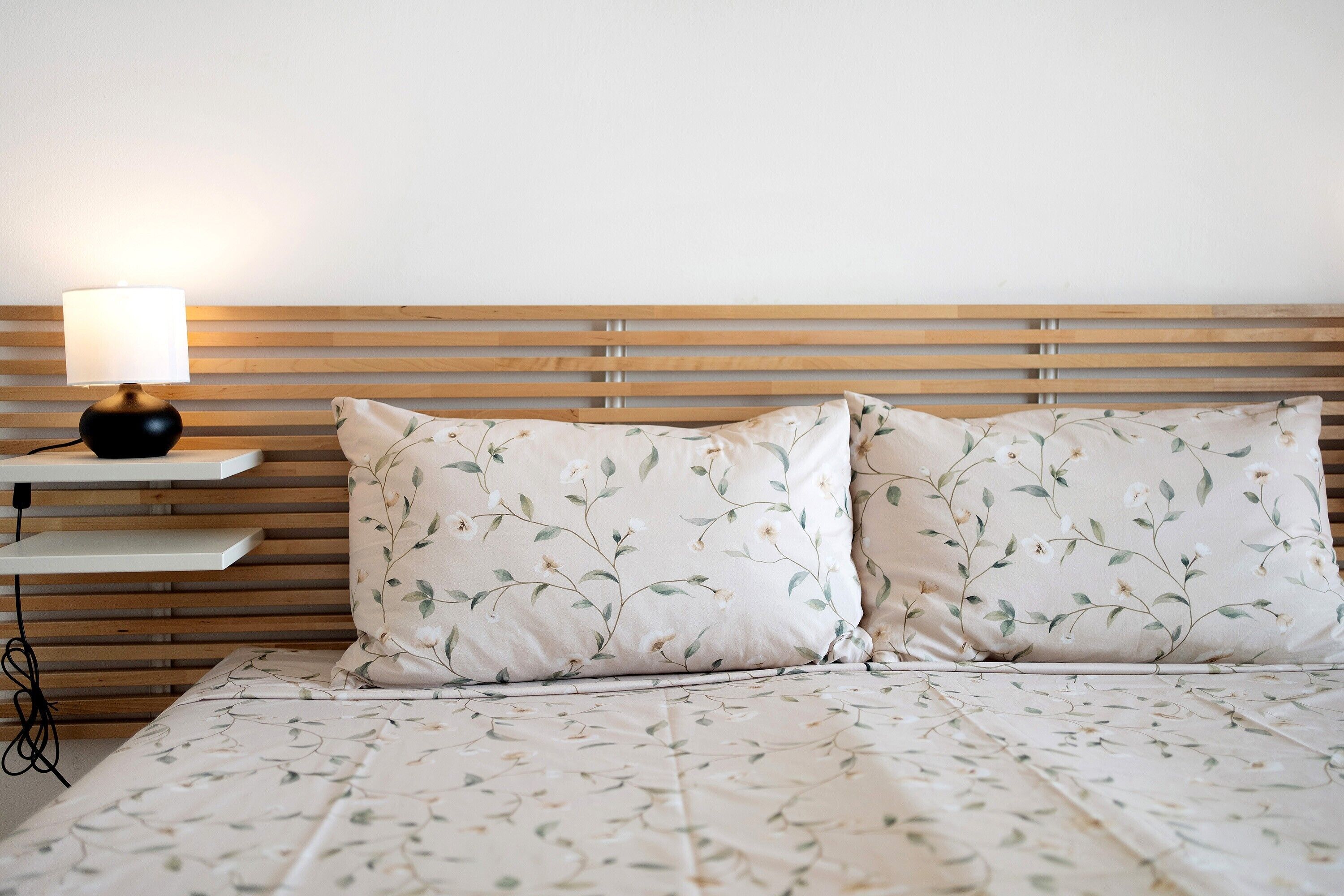 Ein Bett mit blumigem Bettbezug, eine Nachttischlampe und ein hölzernes Kopfteil.