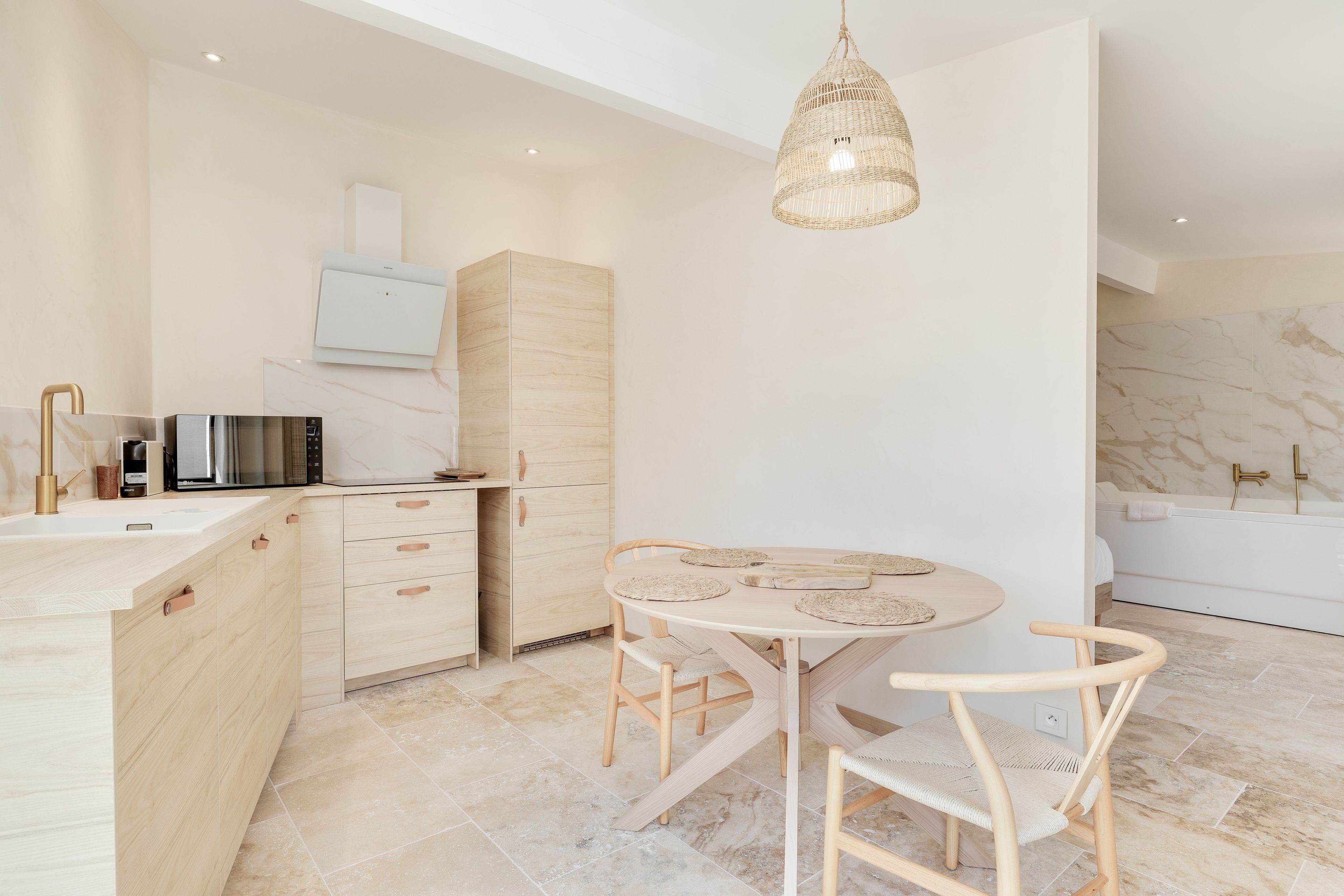 A modern kitchen with a dining area, featuring a round table with chairs, a hanging light fixture, and a built-in oven.