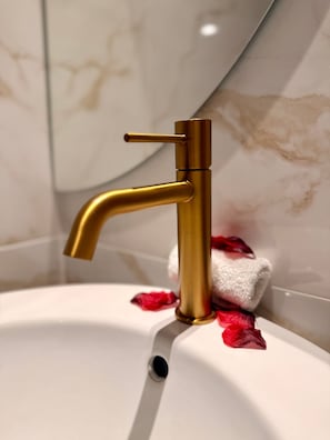 Un lavabo de salle de bain avec un robinet doré, une serviette blanche et des pétales de rose rouges.