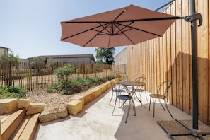 Une terrasse avec une table et des chaises, un parasol et une clôture en bois.