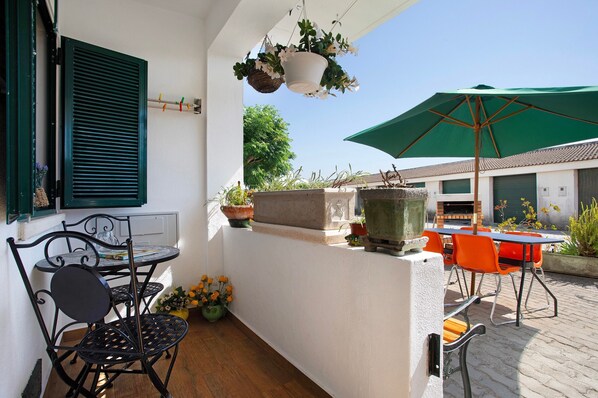 Ein Balkon mit Tisch und Stühlen, einer hängenden Pflanze und einem grünen Sonnenschirm.