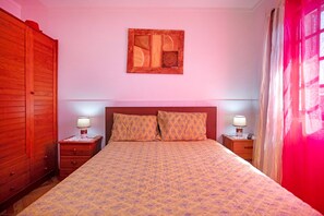 Un dormitorio con una cama, dos mesitas de noche con lámparas, un armario de madera y una obra de arte enmarcada en la pared.