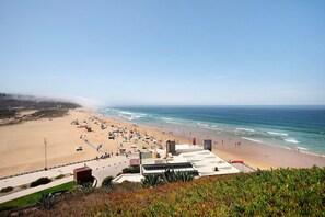 Une plage offrant une vue dégagée sur l’océan, un rivage sablonneux et quelques bâtiments en arrière-plan.