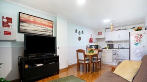 Una sala de estar con televisor, sofá, una mesa de comedor con sillas y una zona de cocina con armarios y refrigerador.