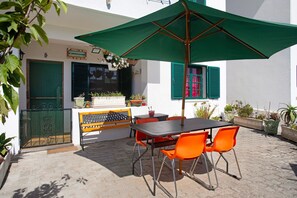 Eine Terrasse im Freien mit Tisch und Stühlen, einem grünen Sonnenschirm und Blumentöpfen.