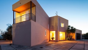 Une maison moderne à deux étages, dotée d’un balcon, de grandes fenêtres et d’une allée pavée.