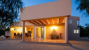 Une maison moderne dotée d’un patio couvert, d’un coin repas et d’une entrée bien éclairée.