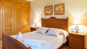 Un lit bien fait, avec une tête de lit en bois, deux tables de chevet avec des lampes et une grande armoire.