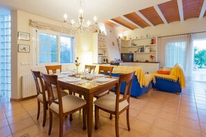Un'area pranzo con un tavolo di legno apparecchiato per quattro persone, un lampadario e una cucina sullo sfondo.