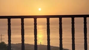 Un coucher de soleil sur une mer calme, avec une rambarde au premier plan.