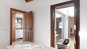 A bedroom with a bed, towels, a wooden door, and a view of a kitchen. - Vacation Home "Centenary Canarian Country House" with Sea View, Private Terrace & Wi-Fi (Punta Gorda)
