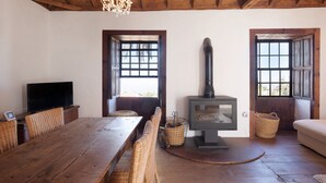 A wooden-floored living room with a TV, a fireplace, wicker furniture, and large windows. - Vacation Home "Centenary Canarian Country House" with Sea View, Private Terrace & Wi-Fi (Punta Gorda)
