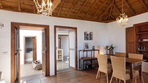 A spacious room with wooden floors, a dining area with wicker chairs, and a chandelier. - Vacation Home "Centenary Canarian Country House" with Sea View, Private Terrace & Wi-Fi (Punta Gorda)