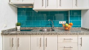 Una cocina con armarios blancos, salpicadero color turquesa, encimera de granito, pileta de acero inoxidable y un frutero.