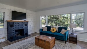 Un salon avec une cheminée, un canapé bleu, une table basse et de grandes fenêtres.