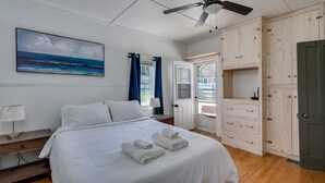 Une chambre à coucher comprenant un lit, un ventilateur de plafond, un tableau, une armoire et une porte donnant sur un balcon.